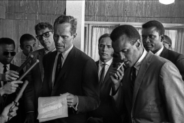 Charlton Heston reading a civil rights declaration on behalf of the Hollywood delegation. Left to right: James Baldwin, Burt Lancaster, Marlon Brando, Harry Belafonte and Sidney Poitier. Washington National Airport, DC. August 28, 1963. Price on request.