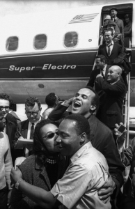 Selma to Montgomery March 1965 Day 4, At the Montgomery Municipal Airport, where a plane load of celebrities arrives. Mrs. King, having greeted Harry Belafonte with an enthousiastic kiss, playfully shares one with Dr. King.