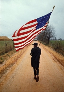 Selma to Montgomery March 1965 Day 4, Will Henry “Do-Right” Rogers with his hand-made flag and home-made pole, on the Rogert Gardner Farm Road, Lowndes County, 23 March 1965. Call for pricing.